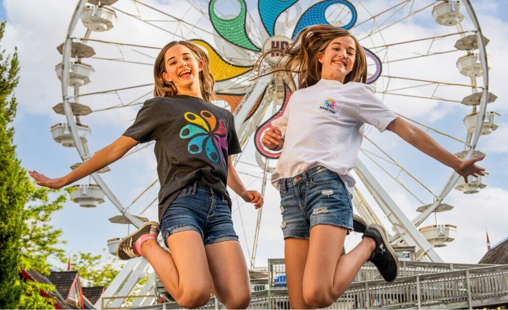 Two girls jumping in front of ferris wheel